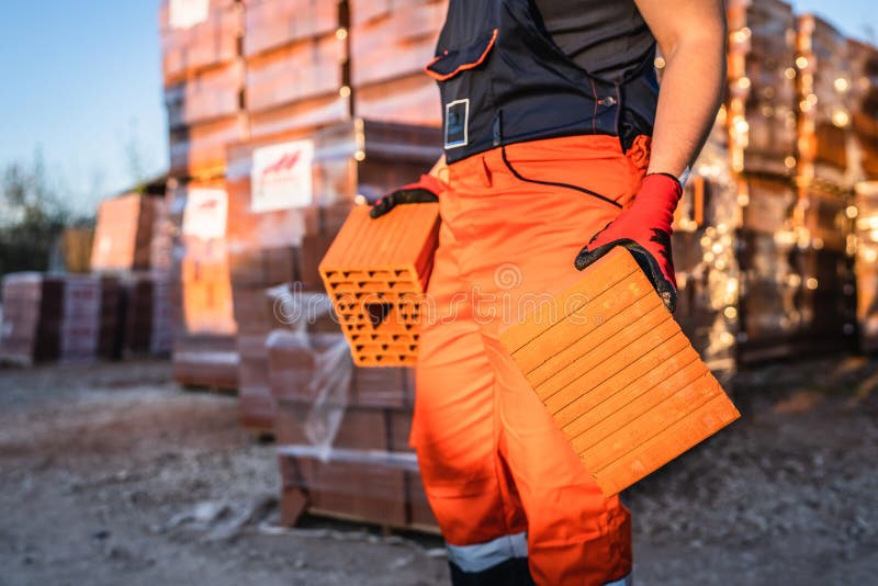 Close up on hands and midsection of unknown man construction worker taking orange hollow clay blocks ar warehouse or construction stock image