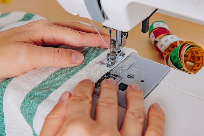 A Close-Up of Hands Operating a Sewing Machine to Craft Beautiful Fabric Designs with Colorful Thread Spools in the Background royalty free stock image