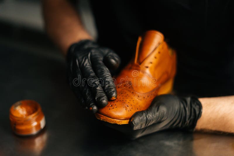 Close-up hands of shoemaker in black gloves rubbing paint on toe cup of light brown leather shoes