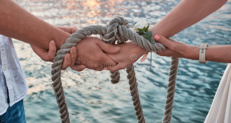 Close-up. Hands tied with sea rope against backdrop of sea water at sunset. An oath with hands as sign of eternal