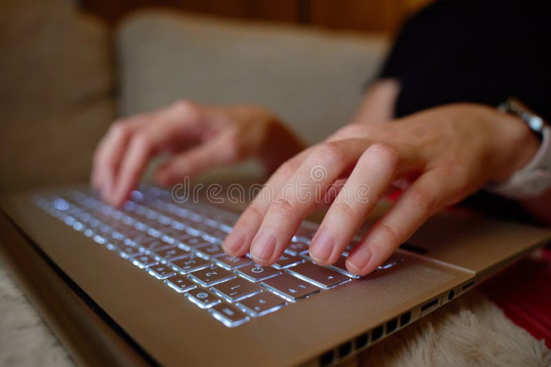 Close up of hands typing on laptop keyboard while sitting on sofa. Concept of remote work