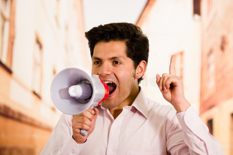 Close up of a handsome man screaming with a megaphone, doing a signal with his hand in a blurred background stock photos Close up of a handsome man screaming with a megaphone, doing a signal with his hand in a blurred background stock photos