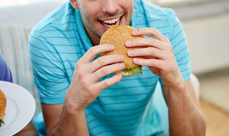 Close Up Of Happy Man Eating Hamburger At Home