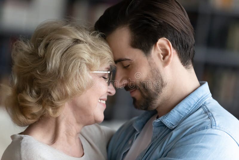 Close up of happy mature m touch forehead enjoy close tender moment with adult son, overjoyed senior 60s mom share intimate family time with grown-up men child, show love and care. Close up of happy mature m touch forehead enjoy close tender moment with adult son, overjoyed senior 60s mom share intimate family time with grown-up men child, show love and care