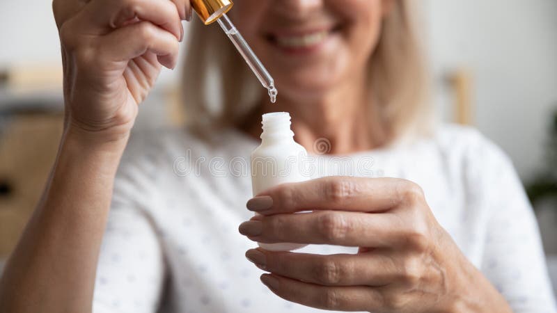 Close up happy older woman opening bottle with essence.