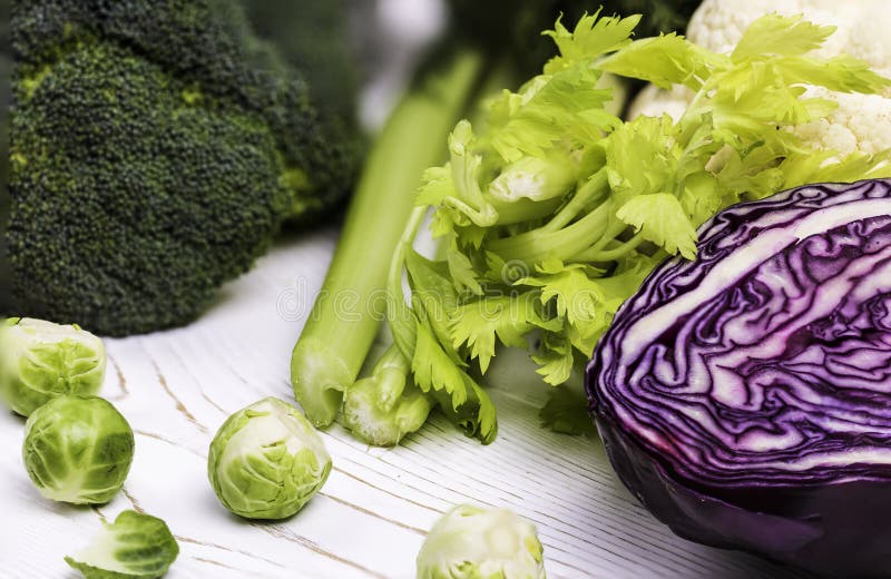 A close-up of the harvest of fresh vegetables on a wooden table: cabbage, broccoli, and Brussels sprouts and red cabbage, celery