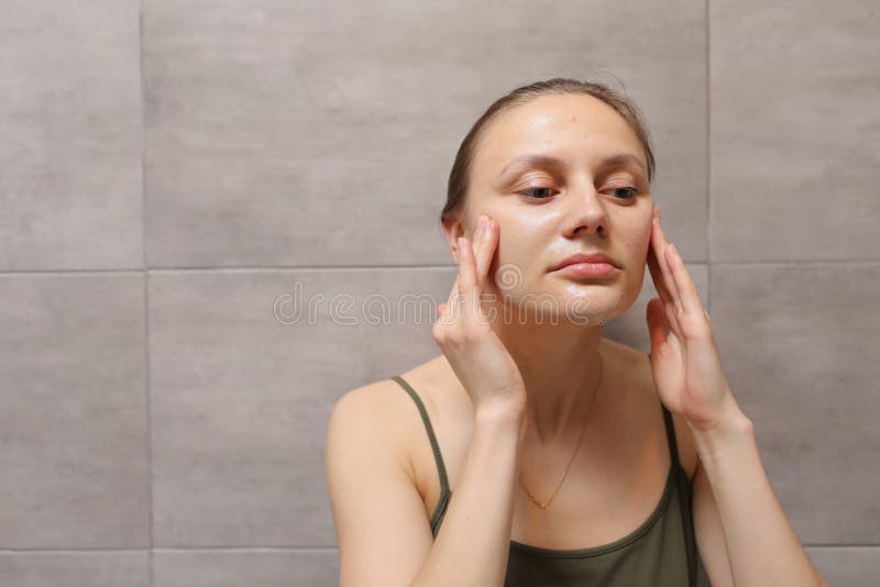 Close Up Headshot Satisfied Young Woman Touching Face Standing In Bathroom Looking At Mirror