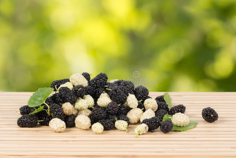 Close-up heap of ripe white and black mulberries with green leaves on table. stock images