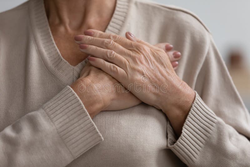 Close up hopeful grateful mature woman keeping hands on chest