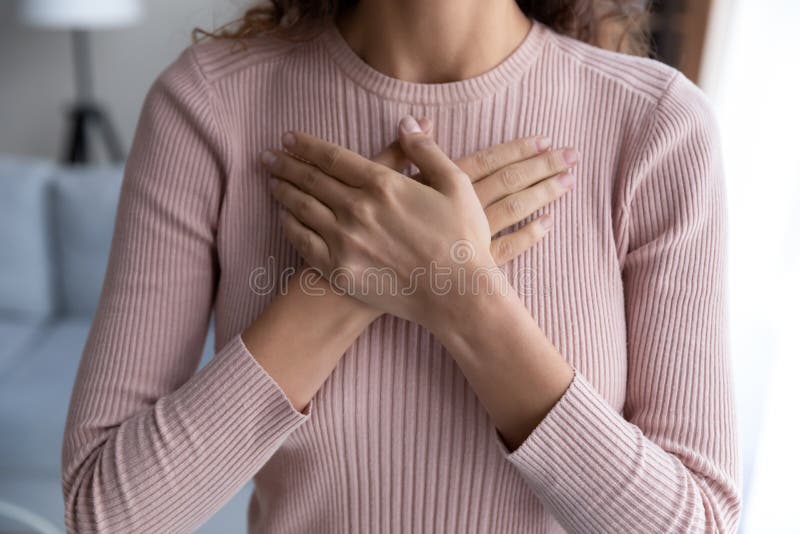 Close up hopeful grateful young woman keeping hands on chest