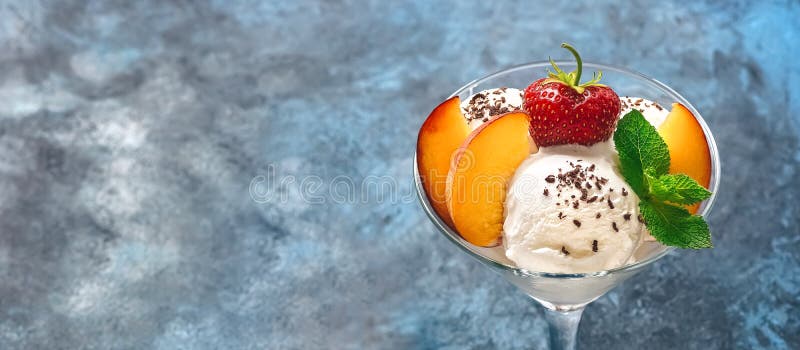 Close-up of ice cream with grated chocolate, strawberries and peach in a glass on a blue rustic background, banner. Summer refreshing dessert. Selective focus, copy space, border.