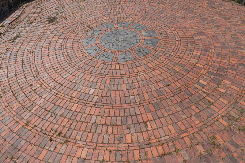 Close-up image of a circular brick floor with concentric circles and a central metal disc, varying in color and size stock photography