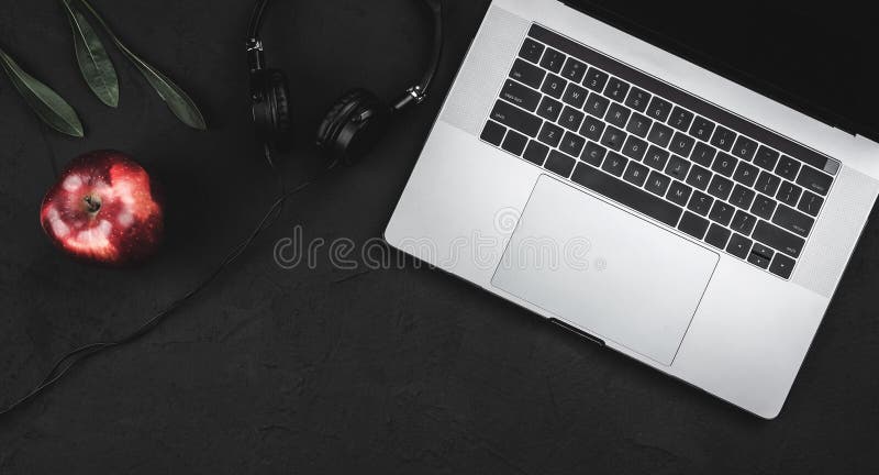 Close-up image of comfortable working place, on the black table lie laptop, headphones and red apple royalty free stock photo Close-up image of comfortable working place, on the black table lie laptop, headphones and red apple royalty free stock photo