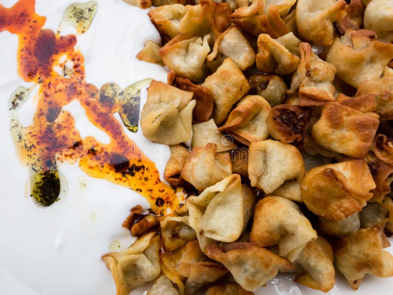 Close up image of fried Turkish Manti with red pepper, tomato sauce, yogurt and mint. Plate of traditional Turkish food. Top view