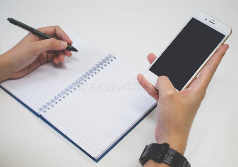 Close up image. A hands with pen writing on notebook and using smartphone at the same time. stock image Close up image. A hands with pen writing on notebook and using smartphone at the same time. stock image