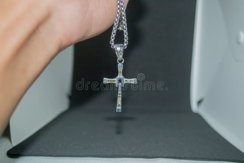 Close-up image of a man holding a silver metal christian cross necklace/pendant or silver metal crucifix necklace/pendant hanging royalty free stock photo