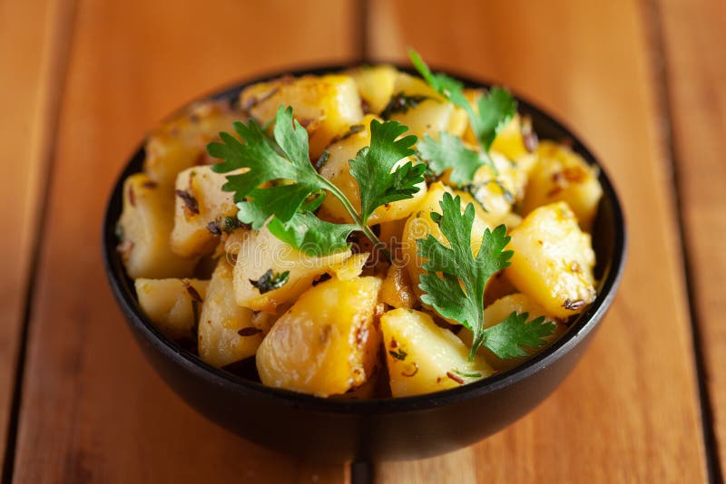 Close-up of Indian vegetarian classic dish Jeera Aloo - Potatoes Flavored with Cumin  garnished with green coriander fresh leaves.