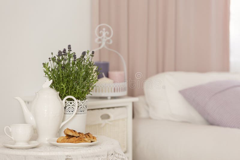 Close-up of kettle, dessert and lavender flowers on table in hotel bedroom interior with cabinet. Real photo concept