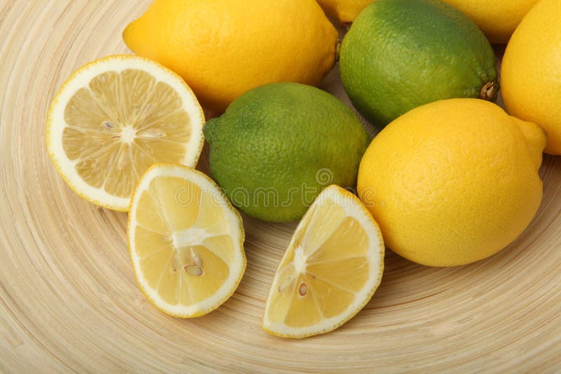 Close-up of lemons and limes on a wooden plate on green background