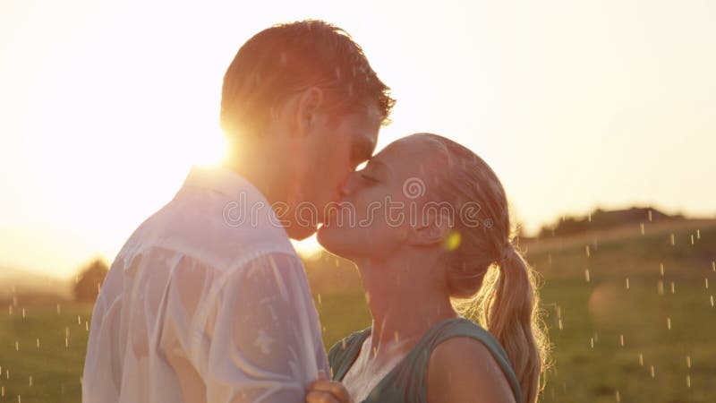 LENS FLARE: Beautiful blonde woman and handsome man kiss in the summer rain.