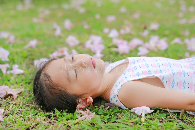 Close up little girl sleeping on green grass with fall pink flower in the garden outdoor