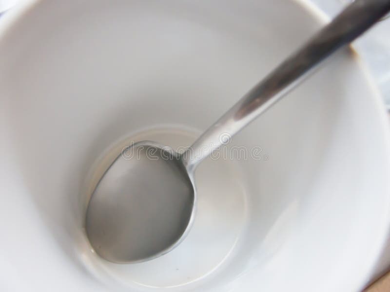 A Close up long silver spoon in white empty coffee cup.