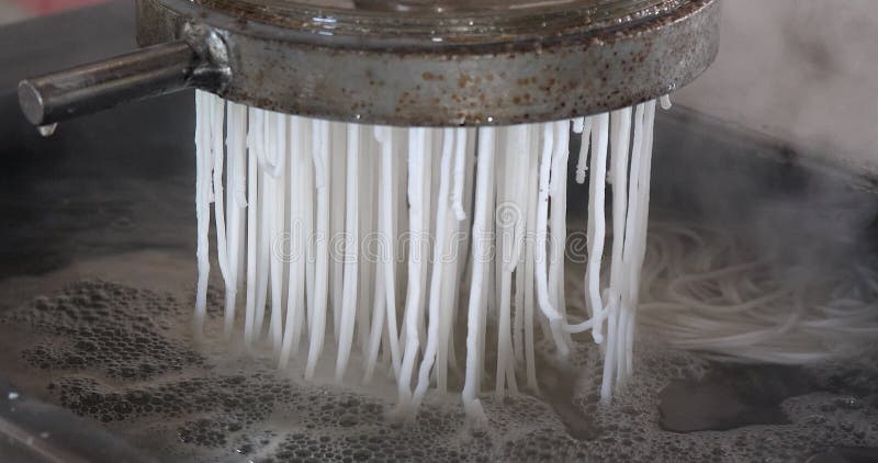 close up of a machine extruding noodles into boiling water.