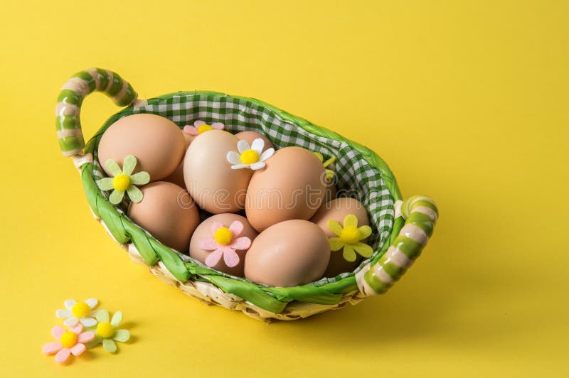 Close up. Easter. Rustic eggs in a wicker basket. The decor of the felt flowers of pastel colors. Yellow background. Copy space royalty free stock photo Close up. Easter. Rustic eggs in a wicker basket. The decor of the felt flowers of pastel colors. Yellow background. Copy space royalty free stock photo