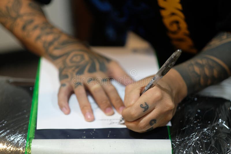 Professional tattooist as he stencils cursive script onto white paper with a pen in preparation for a tattoo session. Professional tattooist as he stencils cursive script onto white paper with a pen in preparation for a tattoo session.