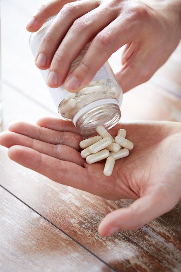 Sport, healthy lifestyle, medicine, nutritional supplements and people concept - close up of man pouring pills from jar to hand