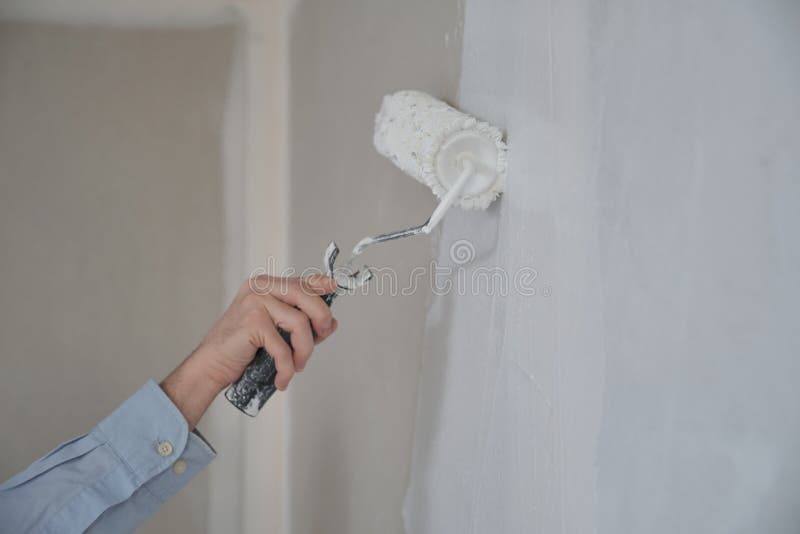 Close-up of mans hand using paint roller with white paint. stock photo