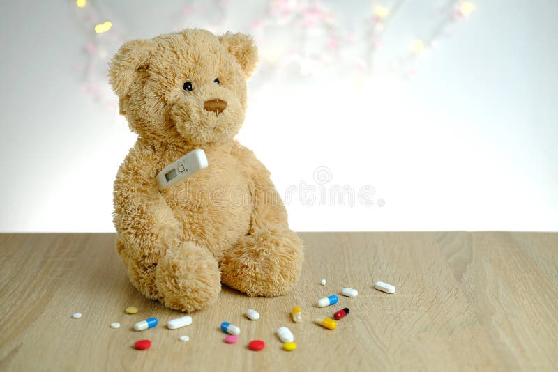 Close-up of many colored pills, medicine, capsules, teddy bear kids toy with stick thermometer, concept of pediatrics, childhood