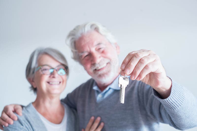 Close up of mature man holding a key of a new home or house or some property of both - couple of seniors and pensioners smiling