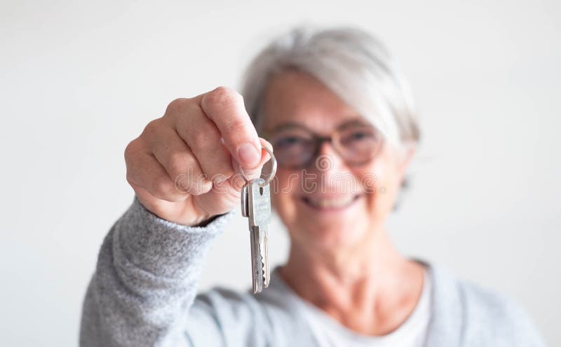 Close up of mature woman holding a couple of keys of her new house or home or some property - indipendent senior.