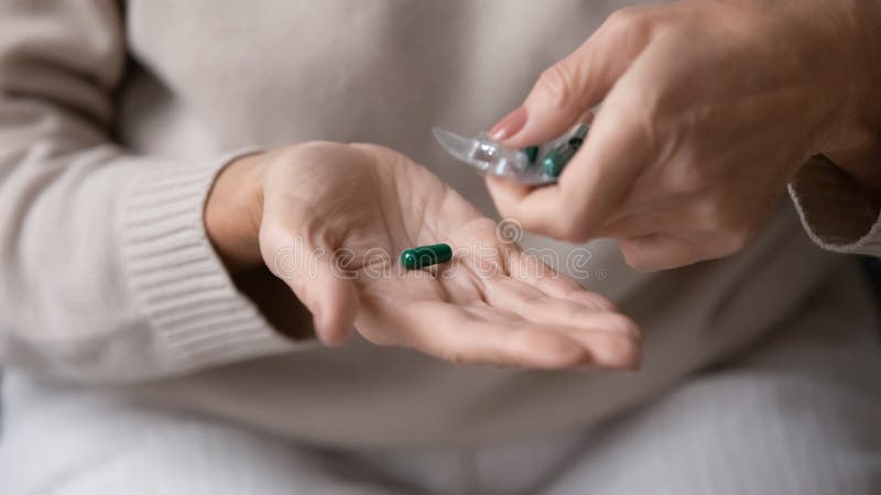 Close up mature senior woman taking pill out of packaging, preparing to take emergency medicine, middle aged female holding supplement or antibiotic, elderly healthcare and treatment concept. Close up mature senior woman taking pill out of packaging, preparing to take emergency medicine, middle aged female holding supplement or antibiotic, elderly healthcare and treatment concept