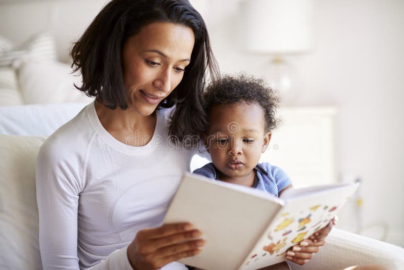 Close up of African American young adult mother sitting in an armchair reading a book with her two year old son, close up royalty free stock photography Close up of African American young adult mother sitting in an armchair reading a book with her two year old son, close up royalty free stock photography