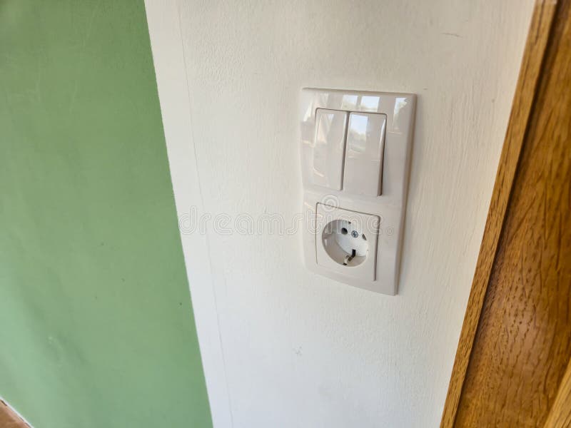 Close-up of a modern electrical socket and switch embedded in a white wall with a green accent. Ideal for articles on ho stock photos