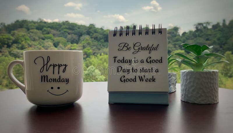 Close up of morning greetings text on coffee cup and quote on notepad - Happy Monday and today is a good day to start a good week. With plants and blurred nature background. Motivational conceptual