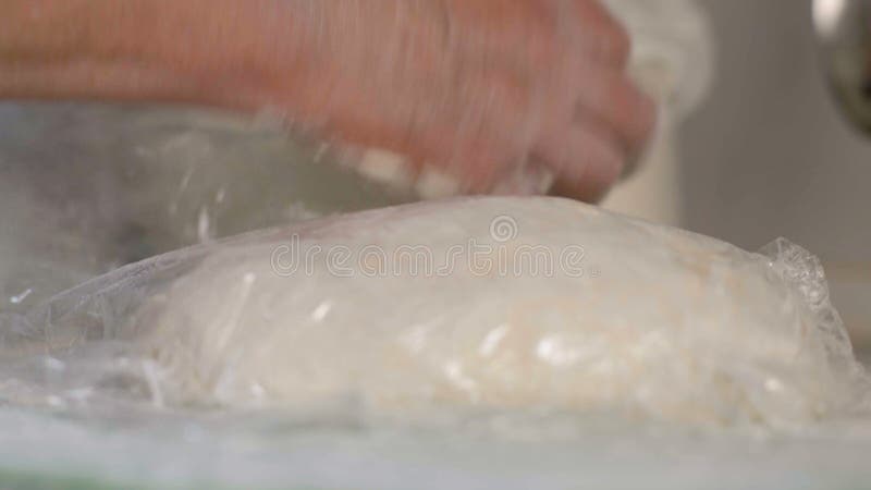 Close-up, mãos de uma mulher idosa coberta com a massa feita malha faixa do alimento em uma mesa de cozinha