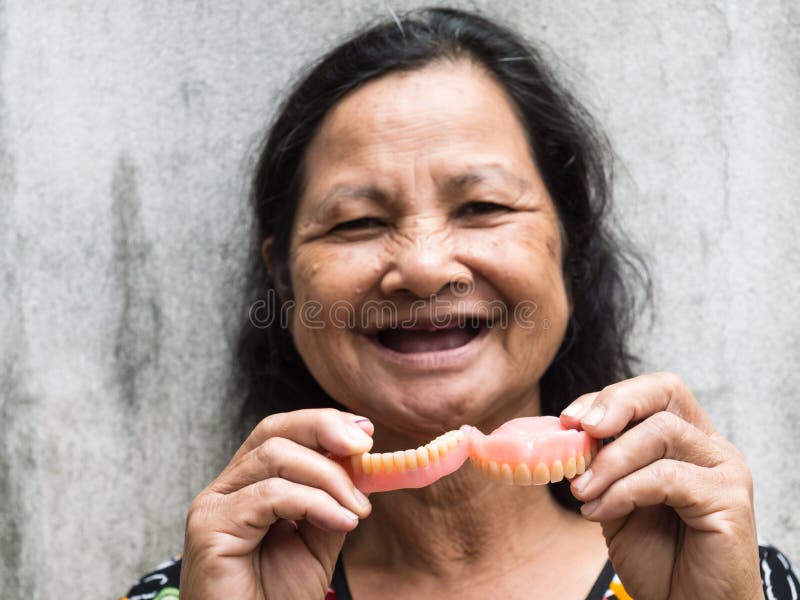 Old thai woman holding false teeth. 