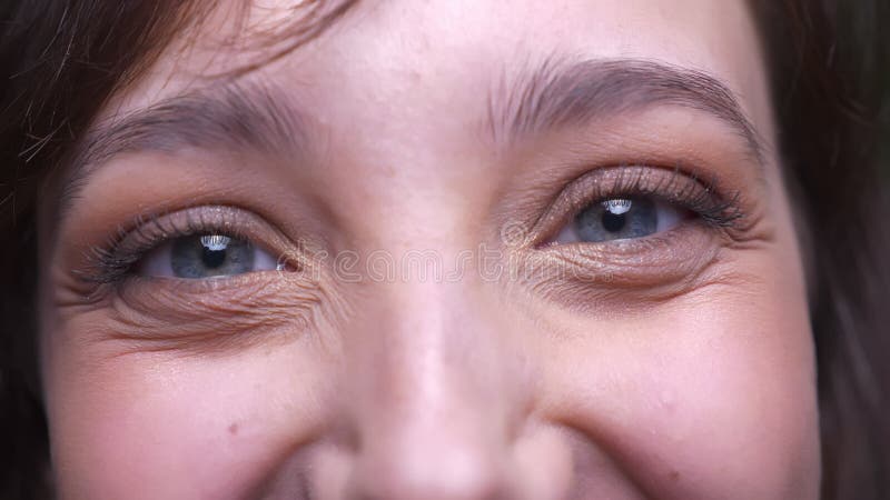 Close-up oog-portret van het donkerbruine vrouwelijke student letten op smilingly en gelukkig in camera op groene achtergrond