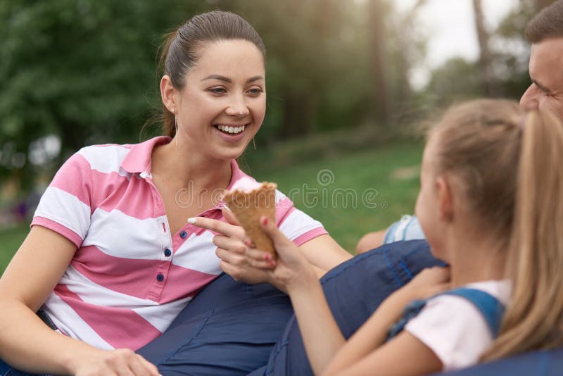 Close up outdoor image of young happy family spending their weekend in park, relaxing while sitting on frameless chair, daughter stock photos Close up outdoor image of young happy family spending their weekend in park, relaxing while sitting on frameless chair, daughter stock photos