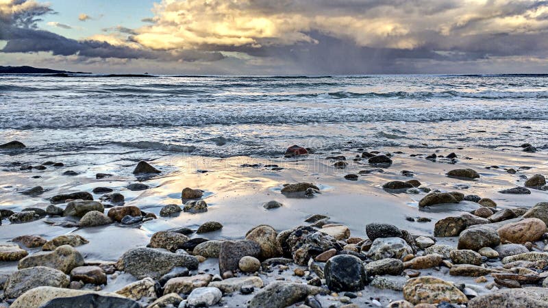 Close up on pebbles bathed by waves on the shore of the calm sea after the storm, with a sky full of threatening clouds