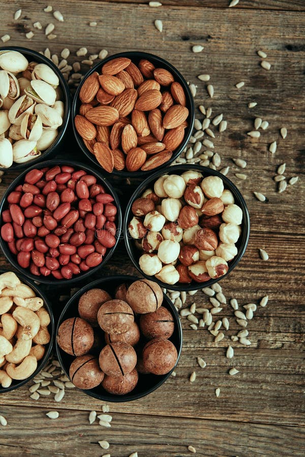 Close up phot of nut mix cashews, pistachios, almonds, macadamia, walnuts and sunflower seeds in bowls on wooden table. High quality photo