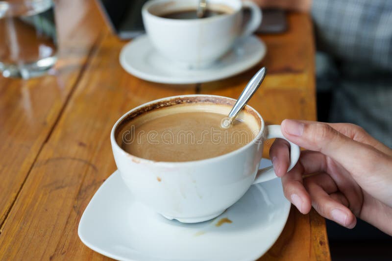 Close-up photo of Asian woman\ s hand He was using his right hand to hold a cup of latte on the table.