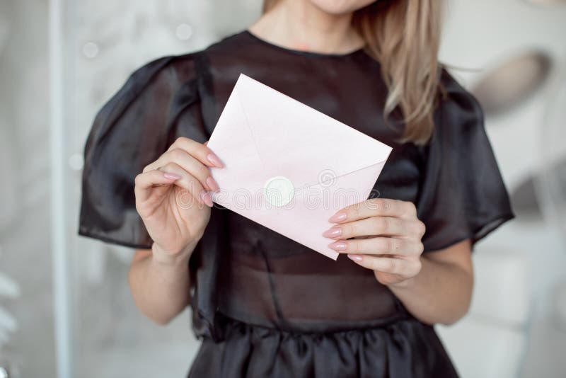 Close-up photo of a female hands holding a pink invitation envelope with a wax seal, a gift certificate, a card, a stock photo Close-up photo of a female hands holding a pink invitation envelope with a wax seal, a gift certificate, a card, a stock photo