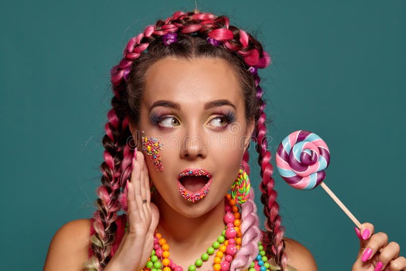Lovely girl with a multi-colored braids hairstyle and bright make-up, posing in studio against a blue background royalty free stock photography Lovely girl with a multi-colored braids hairstyle and bright make-up, posing in studio against a blue background royalty free stock photography