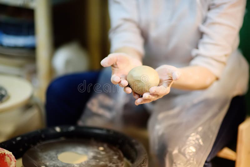 Close-up photo of hands of woman making clay object. Creating a jar or vase of white clay in pottery workshop. The sculptor during her work. Twisted potter`s wheel.