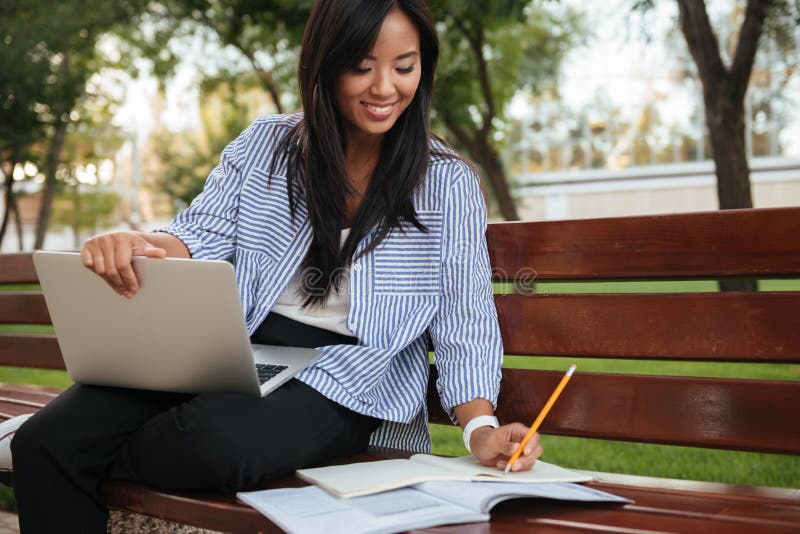 Close-up photo of young smiling asian female student, taking notes, holding laptop, outdoor
