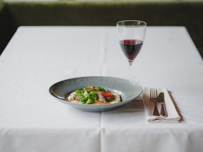 A dinner composition on a blurred restaurant background. A tasty dish next to a glass of red wine. Copy space.